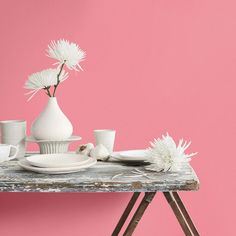 a table topped with white dishes and vases filled with flowers on top of a wooden table