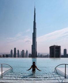 a woman sitting in the middle of a swimming pool with skyscrapers in the background