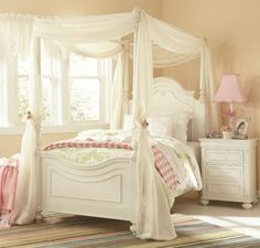 a white canopy bed sitting in a bedroom next to a dresser and lamp on top of a rug