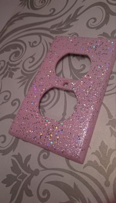 a pink glittered letter sitting on top of a wall next to a floral pattern