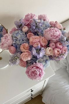 a bouquet of pink and blue flowers sitting on top of a white table next to a mirror