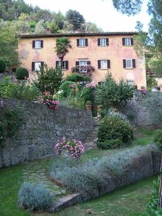 an old house with stone walls and flowers on the front lawn, surrounded by greenery