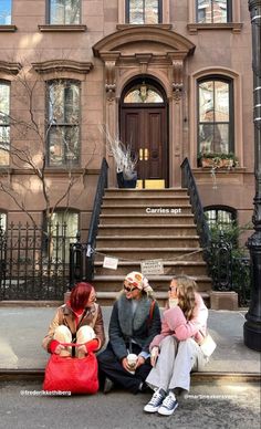 three people are sitting on the steps in front of a building