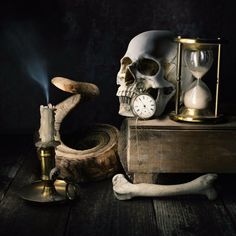 a human skull sitting on top of a wooden table next to an hourglass and candle