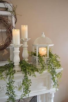 some candles are sitting on top of a mantle with greenery around it and a birdcage