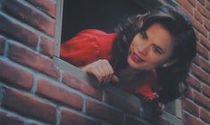 a woman leaning out the window of a brick building with her hand on the ledge