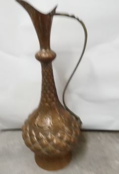 a brown vase sitting on top of a wooden table next to a white sheet covered wall