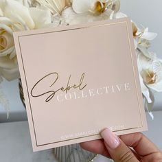 a person holding up a card with the word sparkle collective on it in front of some flowers