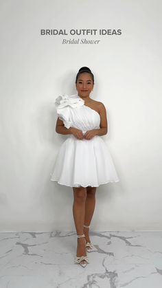 a woman standing in front of a white wall wearing a dress with one shoulder draped over it