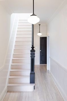 an empty hallway with white stairs and black railing on the second floor is lit by two pendant lights