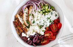 a white bowl filled with meat, vegetables and feta cheese on top of it