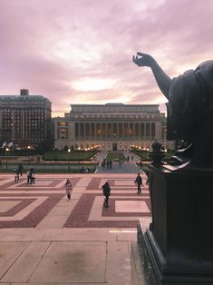 people are walking around in front of a large building with many columns and statues on it