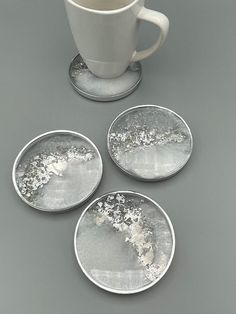 four silver plates and a white cup on a gray surface with the same design as it appears