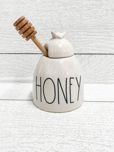 a ceramic honey jar with a wooden spoon in it and the word honey written on it