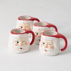 four ceramic santa mugs with red handles on white table top, one has blue eyes and the other has brown nose