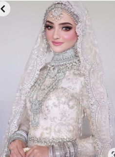 a woman in a white wedding dress and veil with jewelry on her head, holding a bouquet