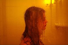 a woman standing in front of a shower with water on her face and long hair