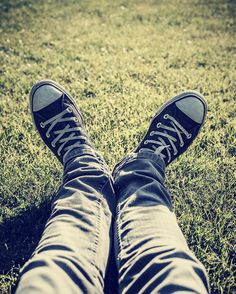 the legs and feet of a person in black sneakers on green grass with sunlight shining through them