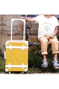 a young boy sitting on a bench next to a yellow piece of luggage with wheels