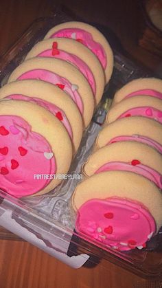 a plastic container filled with lots of pink and yellow cookies covered in white frosting