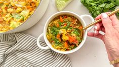 a person holding a spoon in a bowl filled with soup next to other bowls and vegetables