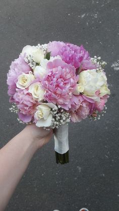 a bridal bouquet being held by someone's hand on the street in front of them