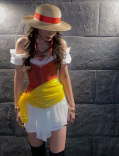 a woman wearing a hat and dress standing in front of a brick wall with her hands on her hips