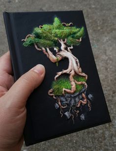 a hand holding up a book with an image of a bonsai tree on it