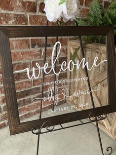 a welcome sign with flowers in front of a brick wall