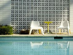 two white chairs sitting next to a pool in front of a wall with geometric designs