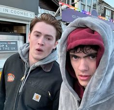 two young men standing next to each other in front of a bus on the street