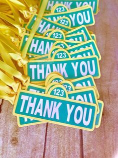 green thank you stickers with yellow ribbons on wooden table next to gold streamers