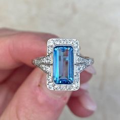 A captivating aquamarine engagement ring that centers a 1.55 carat emerald cut aquamarine gemstone. The aquamarine is Santa Maria color, with a strong blue saturation and a clean crystal. Santa Maria is the best possible color for aquamarines. Surrounding the gemstone is a row of diamonds. Two sections of diamonds adorn the shoulders.
This platinum ring features delicate open-work along the under-gallery. The approximate total diamond weight of this ring is 0.35 carats.
The measurements of the c Blue Square-cut Platinum Ring, Blue Square Cut Platinum Ring, Blue Platinum Rings With Square Cut, Blue Platinum Square Cut Ring, Blue Topaz Ring With Square Cut, Blue Art Deco Jewelry Gia Certified, Emerald Cut Light Blue Topaz Ring With Accent Stones, Light Blue Emerald-cut Topaz Ring With Accent Stones, Light Blue Emerald Cut Topaz Ring With Accent Stones