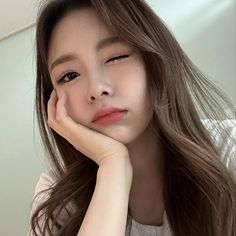 a woman with long brown hair and white shirt posing for the camera while holding her hand to her face