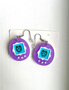 Nostalgia meets style with our Tamagotchi earrings, a playful throwback available at our Etsy store. These quirky accessories pay homage to the iconic virtual pets, blending retro charm with modern fashion. Each pair is a miniature tribute to the beloved Tamagotchi craze, perfect for those who cherish a touch of '90s nostalgia. Elevate your look with these unique earrings - shop now and carry a piece of digital pet history wherever you go! Retro Purple Jewelry For Gifts, Ceramic Tamagotchi, Tamagotchi Accessories, Gameboy Earrings, Tamagotchi Earrings, Tamagotchi Vintage, Virtual Pet, 90s Nostalgia, Creative Jewelry