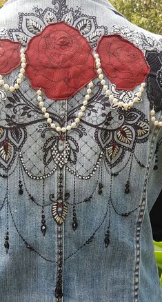 the back of a woman's jean jacket with red roses on it and pearls