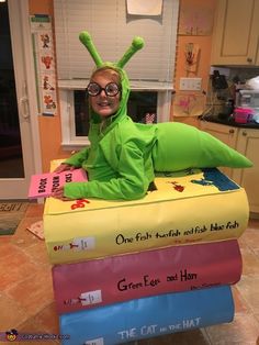 a person in a green bug costume sitting on top of a stack of books while wearing glasses