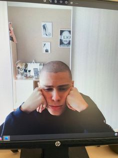 a man sitting in front of a computer monitor with his hand on his head and looking at the screen