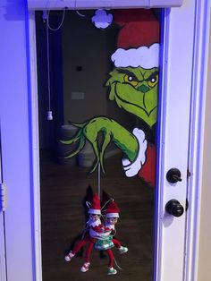 the grinch door decoration is hanging on the front door with two elfs behind it