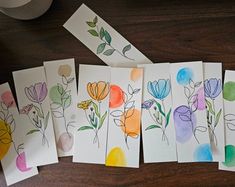 five cards with flowers painted on them next to a roll of tape and a cup