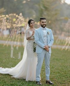 a bride and groom standing in the grass at their outdoor wedding ceremony with lights behind them