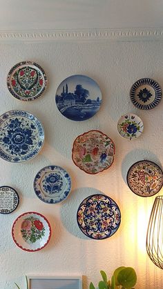 a bunch of plates are hanging on the wall above a table with a vase and potted plant