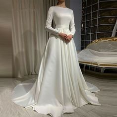 a woman standing in front of a bed wearing a white wedding dress with long sleeves