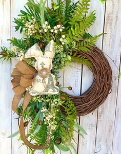 a wreath with a teddy bear on it and greenery around the edges is hung on a white wooden wall