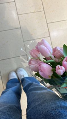 a vase filled with pink tulips sitting on top of a tiled floor next to a person's legs