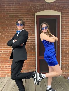 two people dressed in formal wear posing for a photo on a wooden deck with their arms crossed