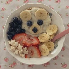 a white bowl filled with fruit and cereal on top of a floral tablecloth covered table