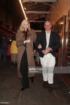 a man and woman are walking down the street at night, one is wearing a brown coat