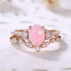 a pink opal and diamond ring sitting on top of a white lace covered table