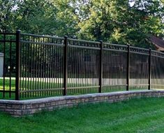 a black metal fence in the middle of a grassy area next to a brick wall